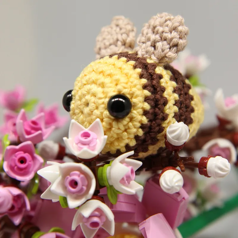 Photograph: the bee from a front three-quarter angle, sitting among pink and white blossoms, its two brown stripes around the yellow body and two beige wings standing up on its back.