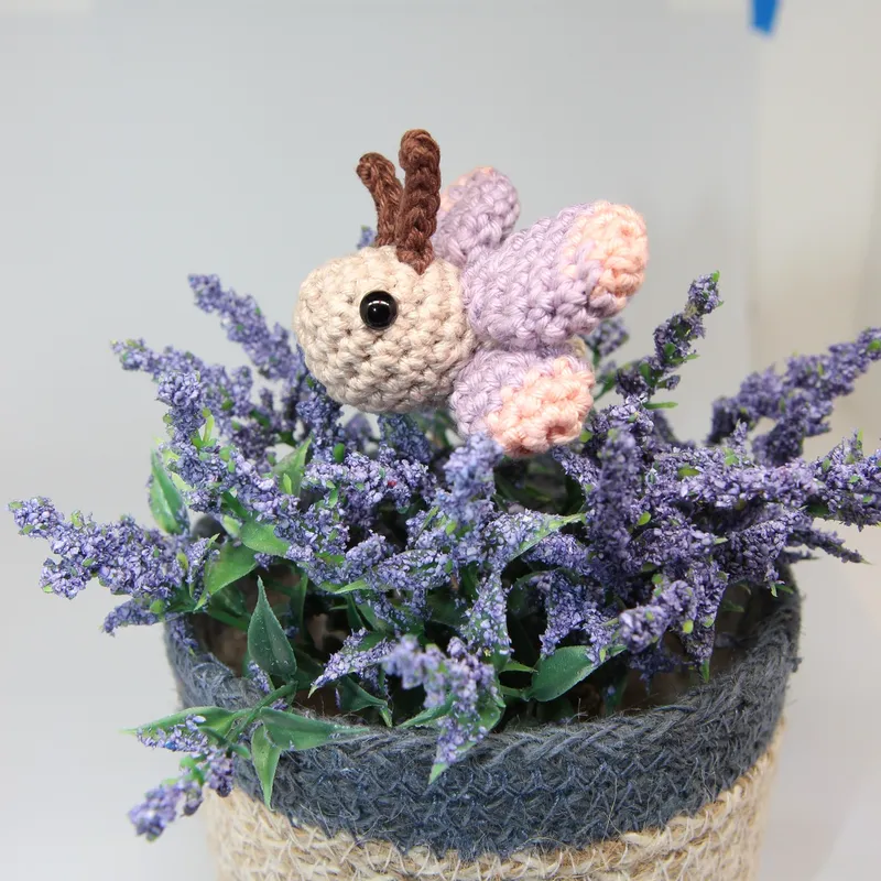 Photograph: the butterfly perched on a pot of lavender, seen from the side, its cream head with a black eye and two brown antennae, the lavender-and-rose wings standing up behind it.