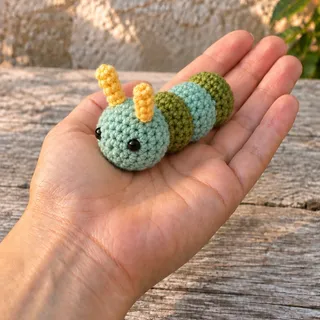 The caterpillar lying across an open palm, an arm extending into the frame from the lower left, a garden plank and wall behind.