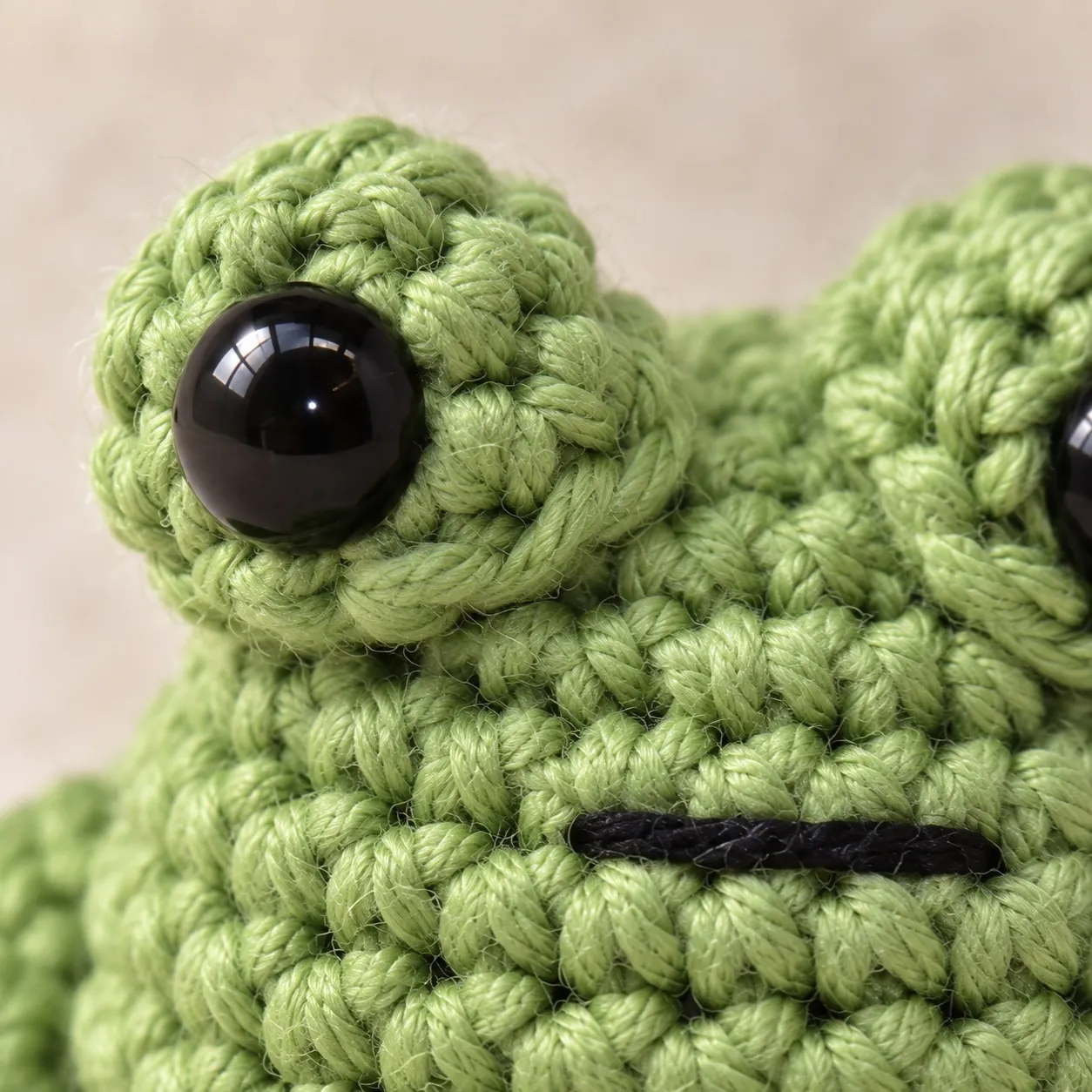 Close view of a crocheted eye cup with a glossy black eye, and a straight black stitch below it.